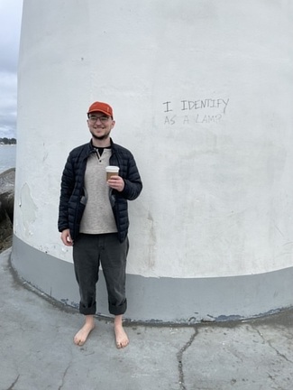 Tyler standing in front of a lighthouse upon which someone has scrawled 'I identify as a Lamp'.